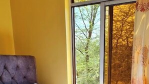 A bed with a quilted white cover, a headboard, and a window with a view of trees. - The Junction Resort Marigat (Marigat)