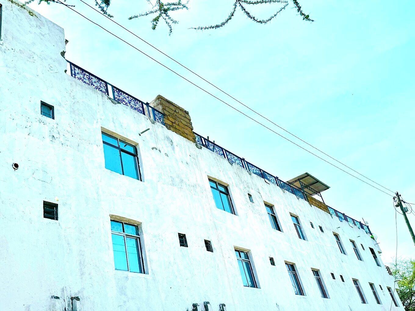 A multi-story building with a white facade, multiple windows, and a balcony with blue railings.
