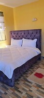 Una cama bien hecha con un cabecero capitonado, una alfombra estampada en el suelo y una lámpara fijada a la pared.