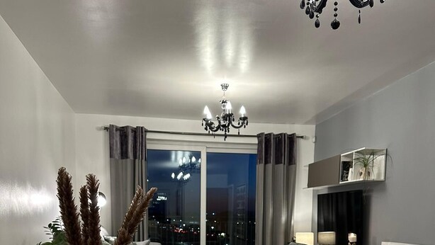 Zona de menjador amb taula de vidre preparada per a quatre, un lampadari i vista a la ciutat per la finestra.