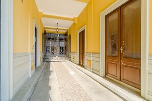 A corridor with a tiled floor, a metal gate, and wooden doors. - GuestHost - Cozy Central Apartment in Turin (Turin)