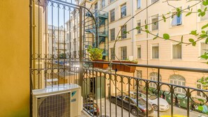 A balcony with a metal railing, a window, and a view of parked cars and buildings. - GuestHost - Cozy Central Apartment in Turin (Turin)