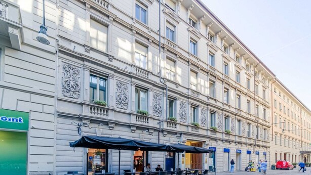 A historic building with ornate architectural details, outdoor seating, and a storefront with a green sign. - GuestHost - Cozy Central Apartment in Turin (Turin)