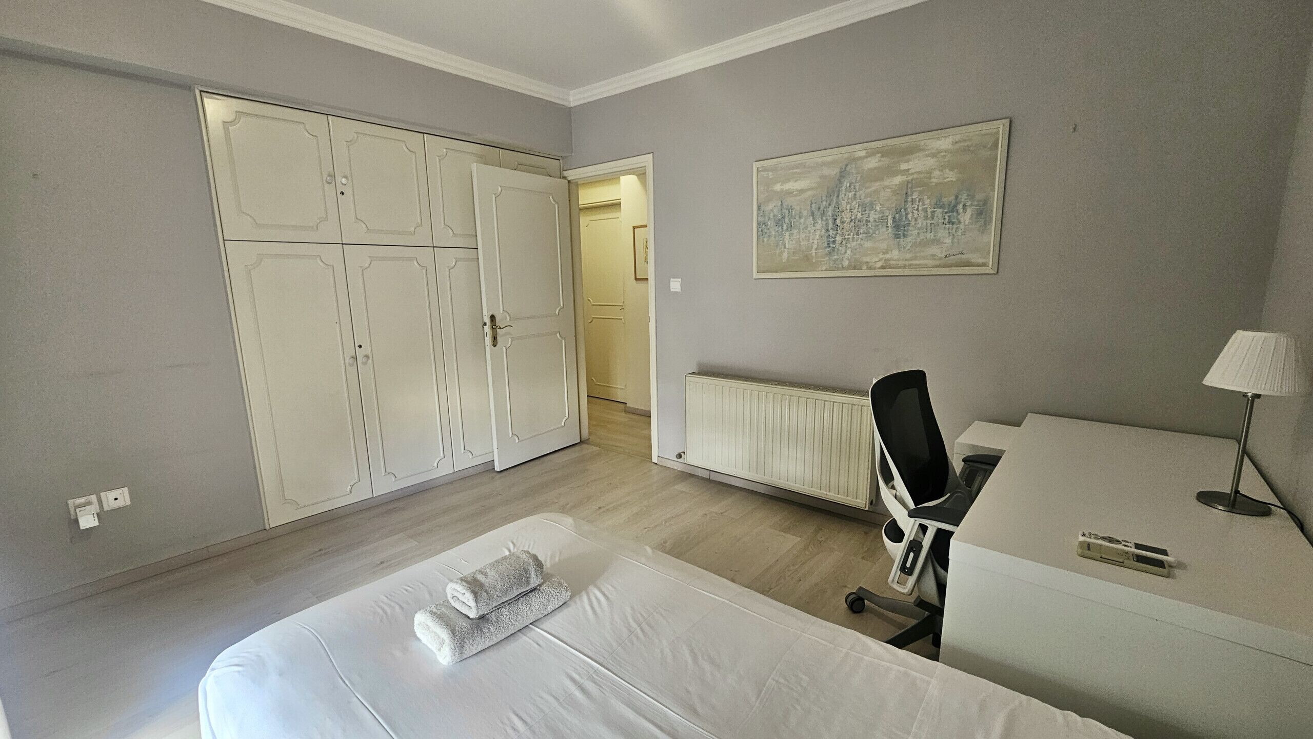 Una habitación de hotel con cama, escritorio, silla, radiador y un cuadro en la pared.