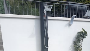 A black outdoor shower with a hose, a control panel, and a safety sign.