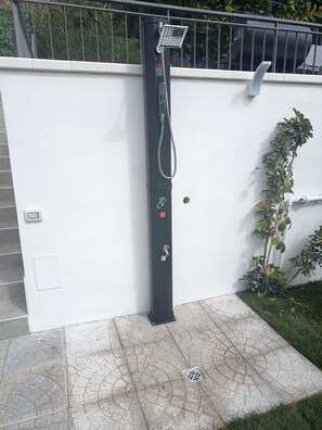 Une douche extérieure noire, équipée d’un tuyau d’arrosage, d’un panneau de commande et d’un panneau de signalisation de sécurité.