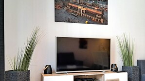Un soggiorno moderno con una televisione a schermo piatto su un mobile bianco, affiancato da due grandi piante in vaso.