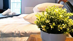Una camera d'albergo con un letto, una pianta in vaso, un quadro appeso e una finestra con tende.