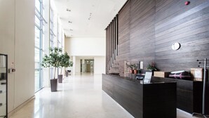 Un área de recepción moderna con un mostrador de madera oscura, plantas en macetas y una puerta de cristal que da a otra habitación.