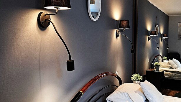 Un dormitorio moderno con una cama, una mesita de noche con lámpara, un espejo y una planta pequeña.