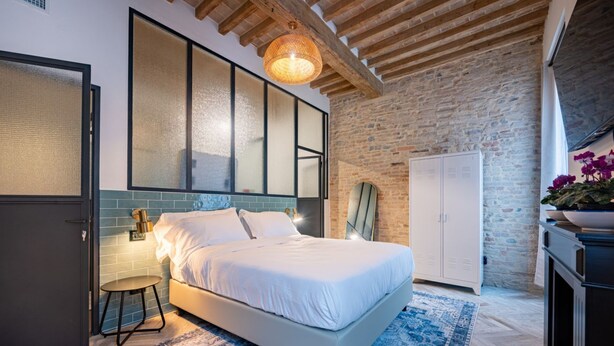 A bedroom with a bed, a nightstand, a wardrobe, and a large window with blinds.