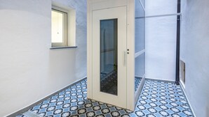 A narrow hallway with a patterned floor, a door with a glass panel, and a small window.