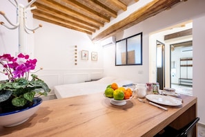 A room with a wooden table, a potted plant, a fruit bowl, and a bed.