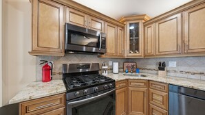 Una cocina con armarios de madera, un microondas de acero inoxidable, una estufa a gas y un lavavajillas.