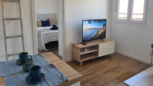Ein Zimmer mit einem Bett, einem Fernseher auf einem Holzständer, einer Leiter und einem Tisch mit Tassen und einem Wasserkocher.