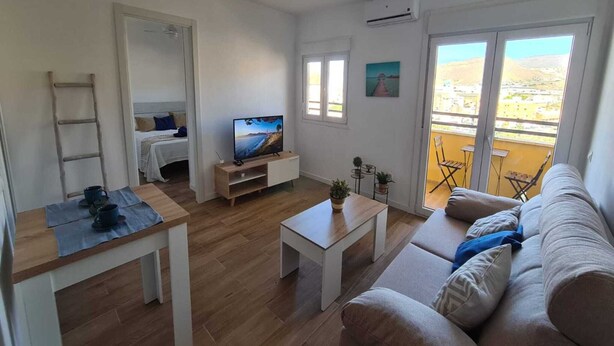 Ein Wohnzimmer mit einer Couch, Couchtisch, Fernseher und einem Balkon mit Gartenmöbeln.