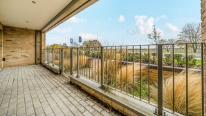 Un balcon donnant sur un jardin aménagé et un ciel dégagé.
