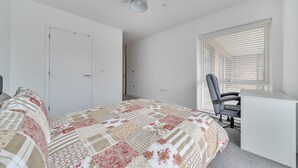 Une chambre avec un lit, un bureau et une chaise. Il y a une fenêtre avec des stores.