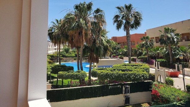 A balcony with a view of a pool, palm trees, and a building in the background. - Seaside apartment in Vera with terrace (vera)