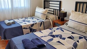A hotel room with two beds, each with a blue bedspread and matching pillows. There is a nightstand with a lamp and a power outlet on the wall. - Seaside apartment in Vera with terrace (vera)