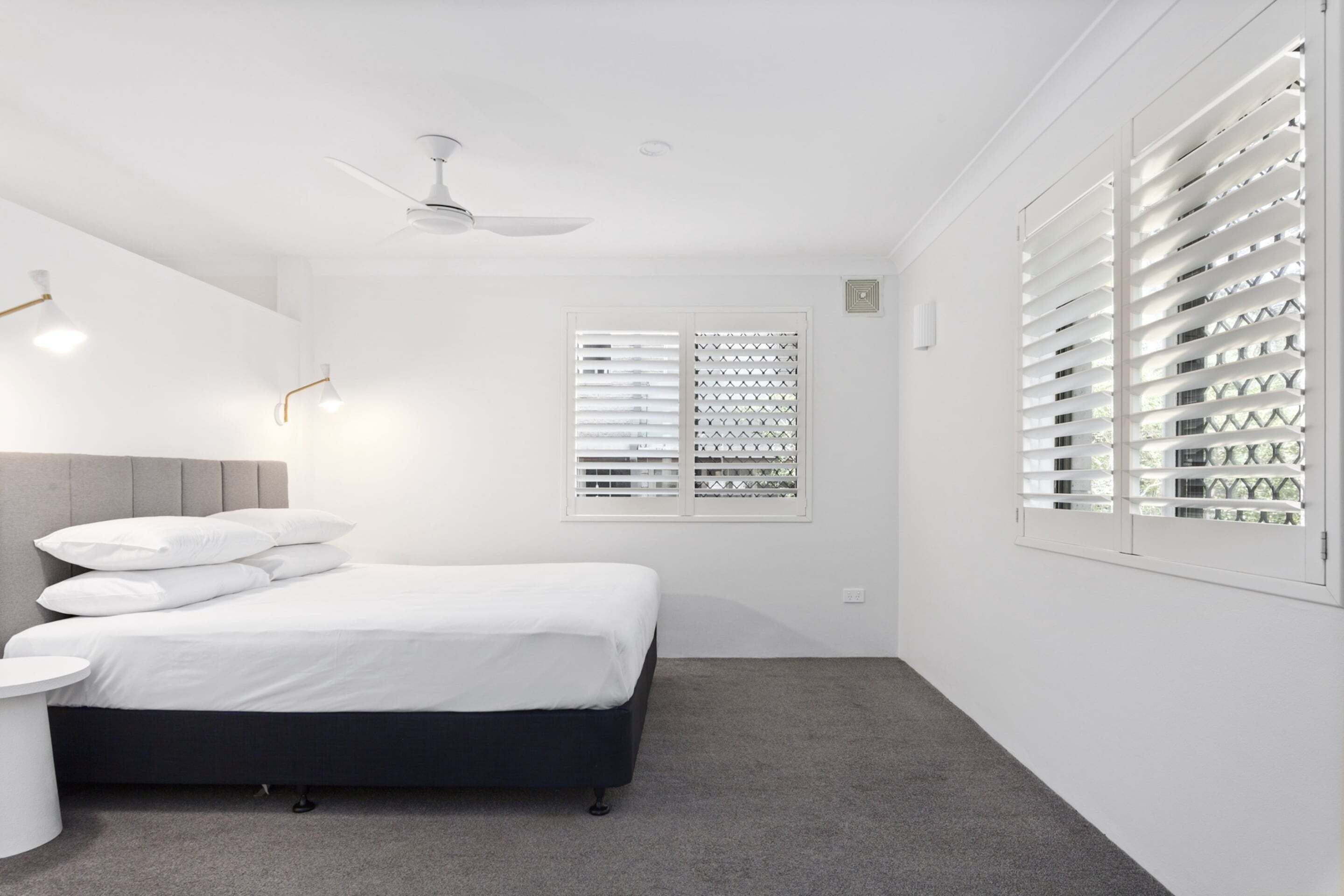 A bedroom with a bed, a bedside table, a ceiling fan, and a window with blinds.
