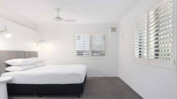 A bedroom with a bed, a bedside table, a ceiling fan, and a window with blinds.