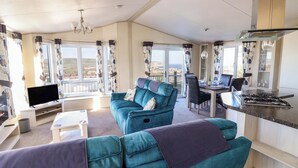A spacious living area with a sofa, a dining table, and a kitchen area. - 91 Swanage Coastal Park (Swanage)