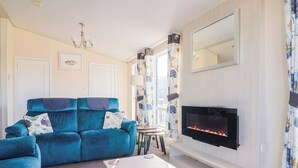 A living room with a blue sofa, a white coffee table, a fireplace, and a large mirror on the wall. - 91 Swanage Coastal Park (Swanage)
