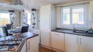 A modern kitchen with a gas stove, white cabinets, a built-in oven, and a window with blinds. - 91 Swanage Coastal Park (Swanage)
