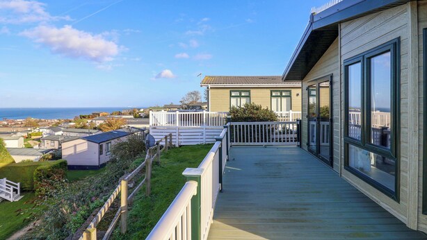 A wooden deck with a view of the sea, a white fence, and a building with large windows. - 91 Swanage Coastal Park (Swanage)