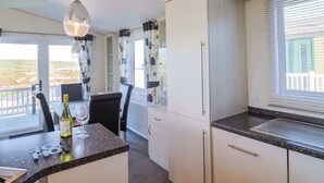 A modern kitchen with white cabinets, a granite countertop, and a dining area with a table and chairs. - 91 Swanage Coastal Park (Swanage)