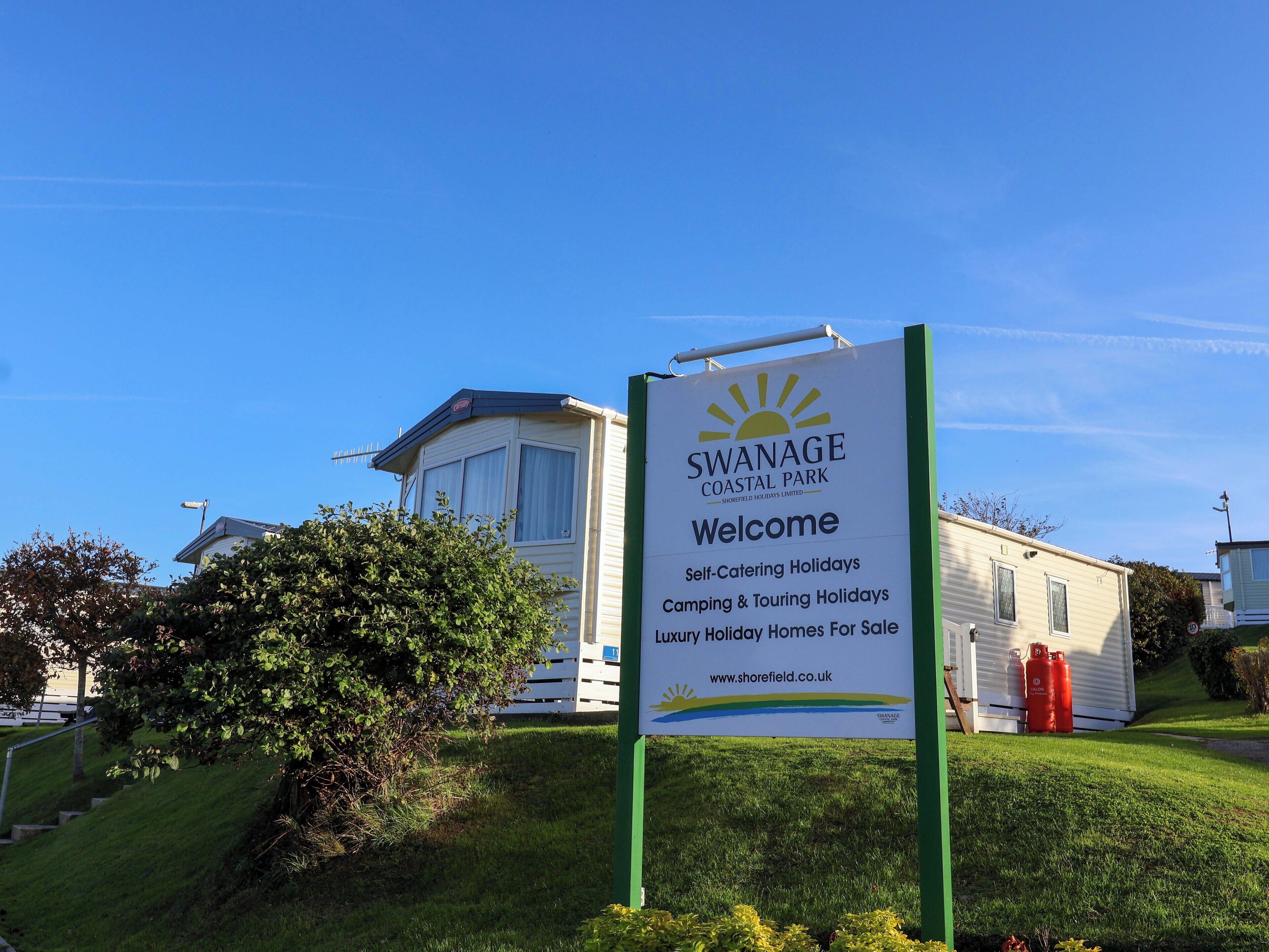 A sign for Swanage Coastal Park welcoming visitors, indicating self-catering holidays, camping and touring holidays, and luxury holiday homes for sale.