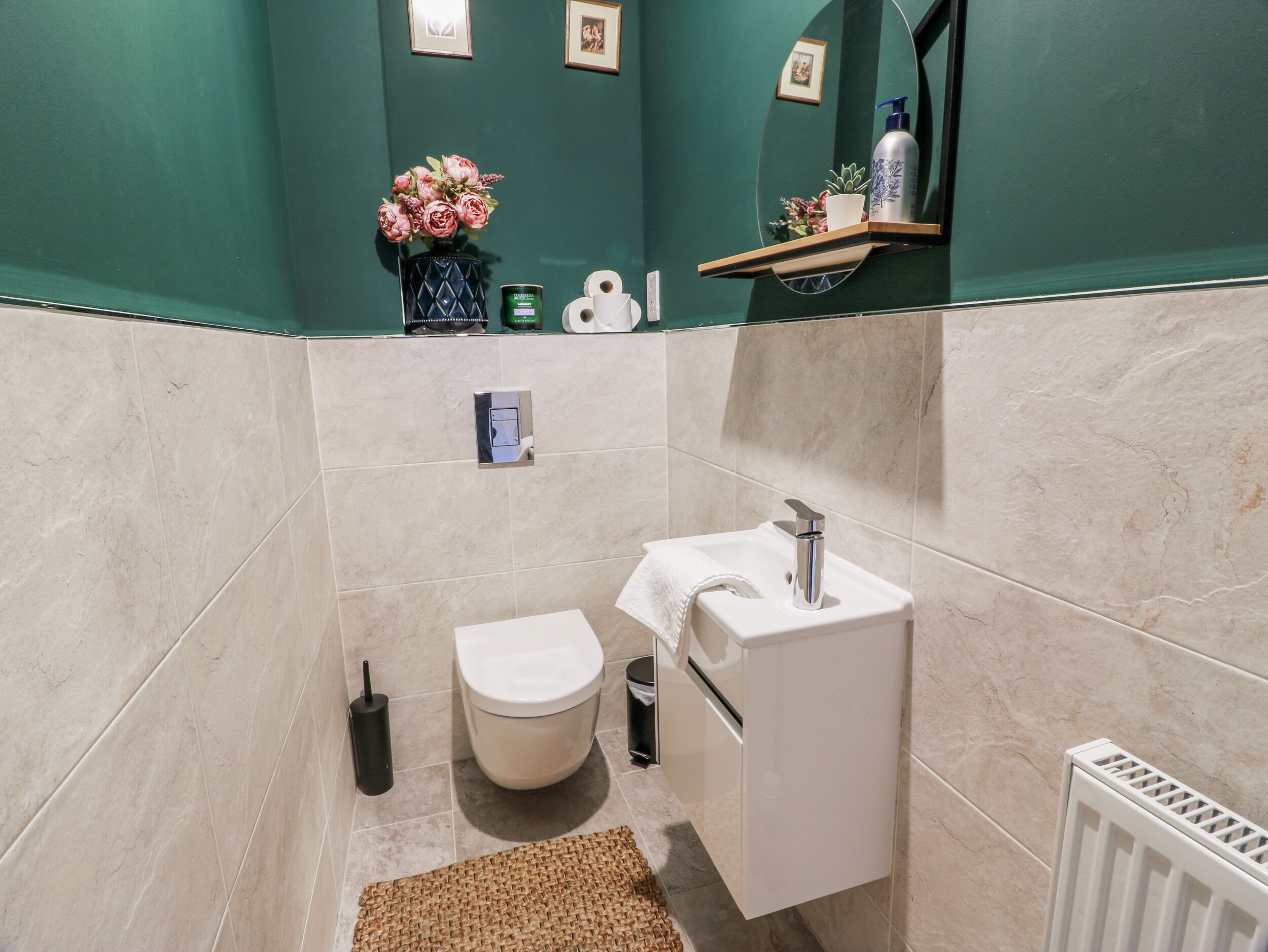 Une salle de bain avec des toilettes, un lavabo et un miroir. On y trouve un porte-serviettes et une petite étagère avec des articles de toilette.