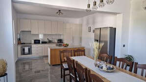 Una cocina moderna con zona de comedor, que incluye una isla central, sillas de madera y un refrigerador de acero inoxidable.