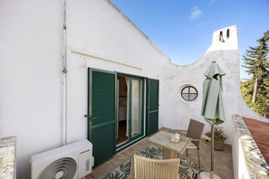 A small patio area with a table, chairs, an air conditioning unit, and a potted plant.