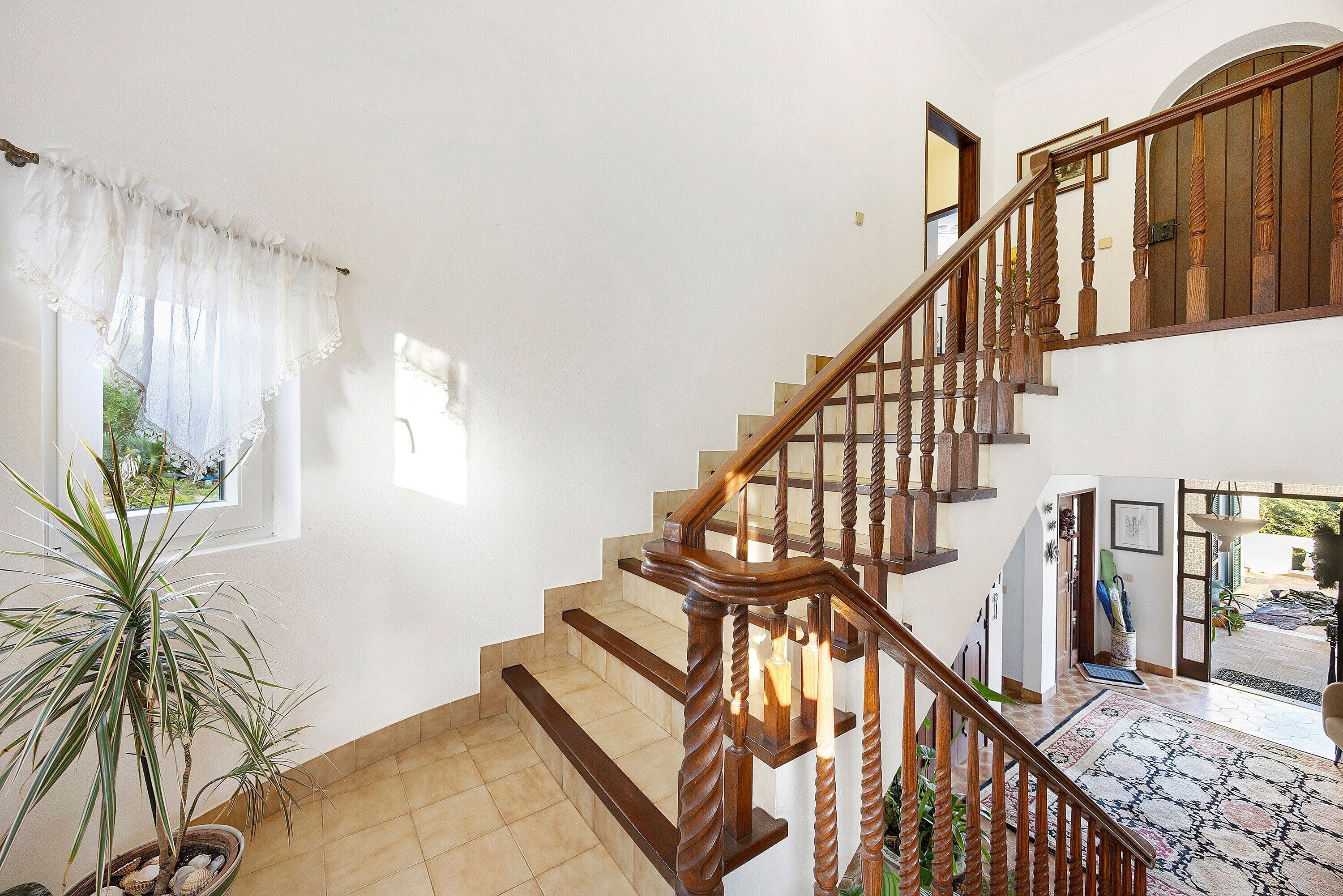 A staircase with wooden balusters, a potted plant, and a view of the outdoors.