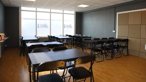 Ein Konferenzraum mit mehreren Tischen und Stühlen, großen Fenstern mit Blick und einer Wand mit Muster.