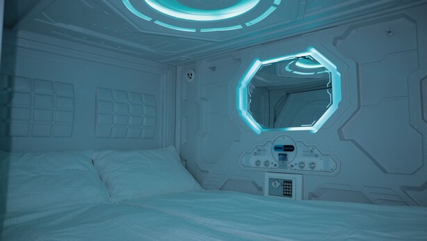 Ein futuristisches Schlafzimmer mit einer zentralen Bedienkonsole, einem sechseckigen Spiegel und einem Bett mit weißer Bettwäsche.