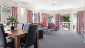 A spacious living area with a dining table, sofas, and a ceiling fan. - Beachside 2-bed Apartment With Secure Parking (Hervey Bay)