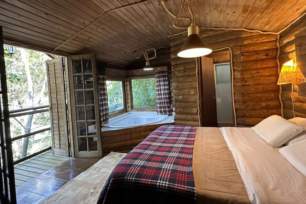 Een chalet met een houten interieur, een bed met een geruite deken, een raam met uitzicht op bomen en een houten plafond.