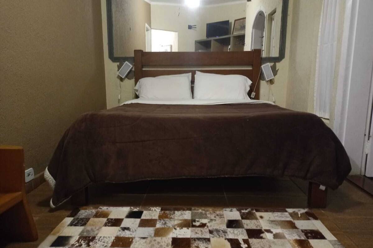 Een slaapkamer met een houten bed, een geruit vloerkleed en een spiegel aan de muur.