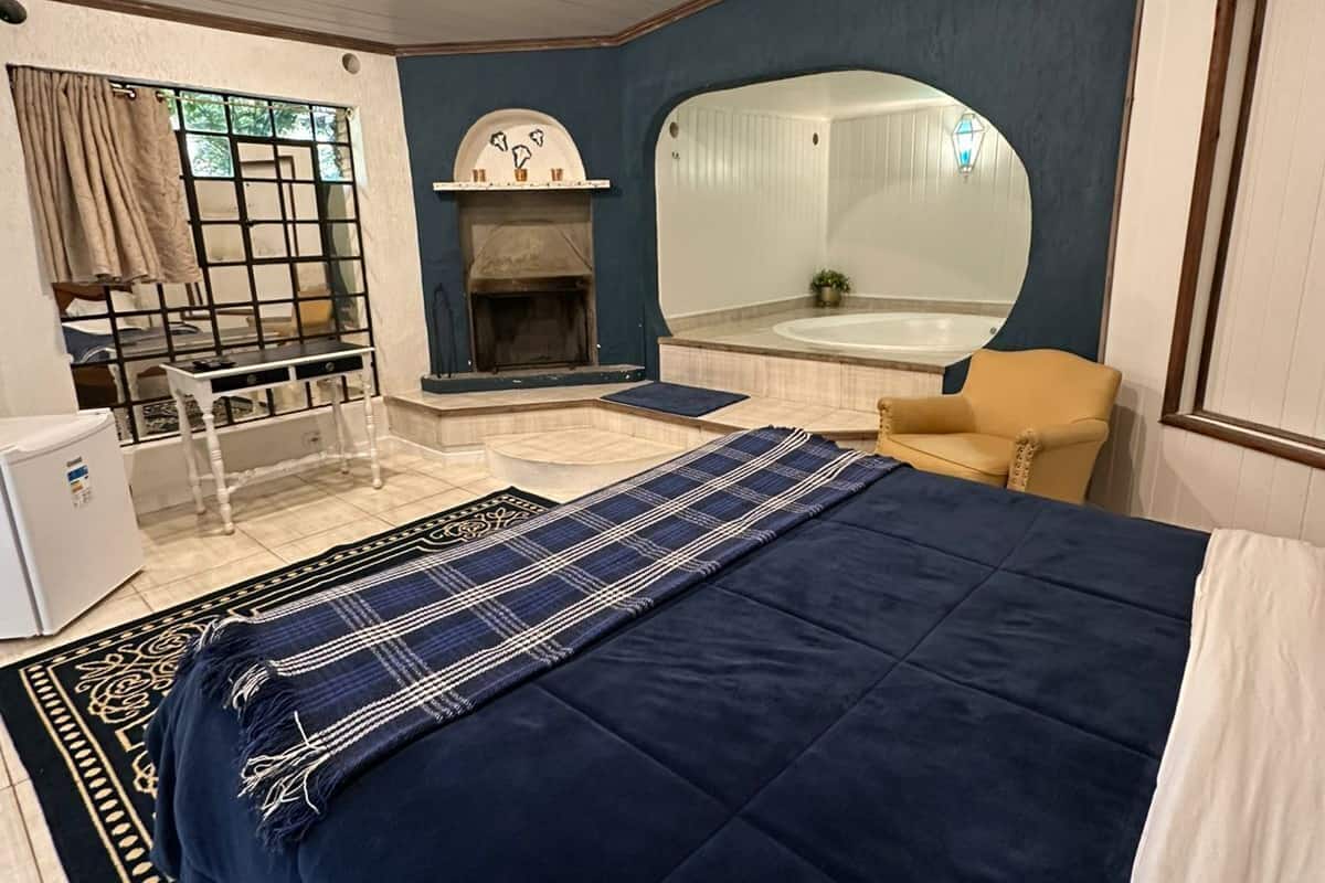 Een slaapkamer met een bed, een stoel, een open haard en een grote spiegel.