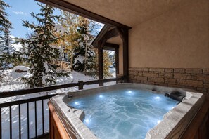 A hot tub with stone walls and a wooden deck, surrounded by snow-covered trees.