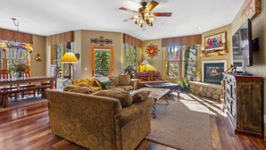 A spacious living room with a fireplace, a ceiling fan, and a dining area with a wooden table and benches. - Ski •Soak •Savor Haven – Private Hot Tub, Private Garage - Walk to Lifts & Town (Breckenridge)