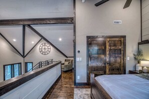 A bedroom with a large bed, a wooden door, and a staircase leading to a loft area with a clock. - Luxury Mountain Lodge | Views, Hot Tub & Firepit (Blue Ridge)
