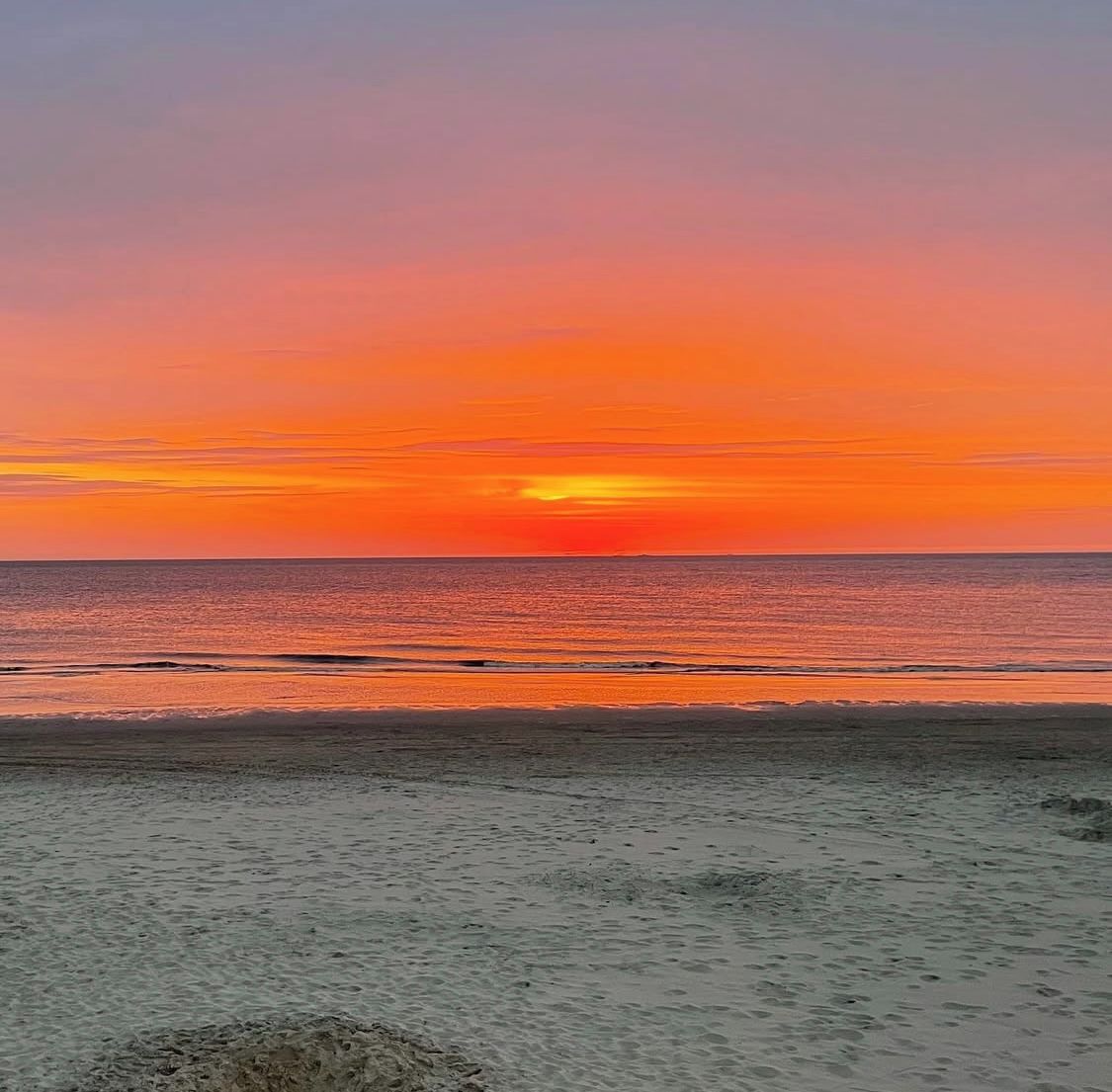 Une plage avec un coucher de soleil sur l’océan.