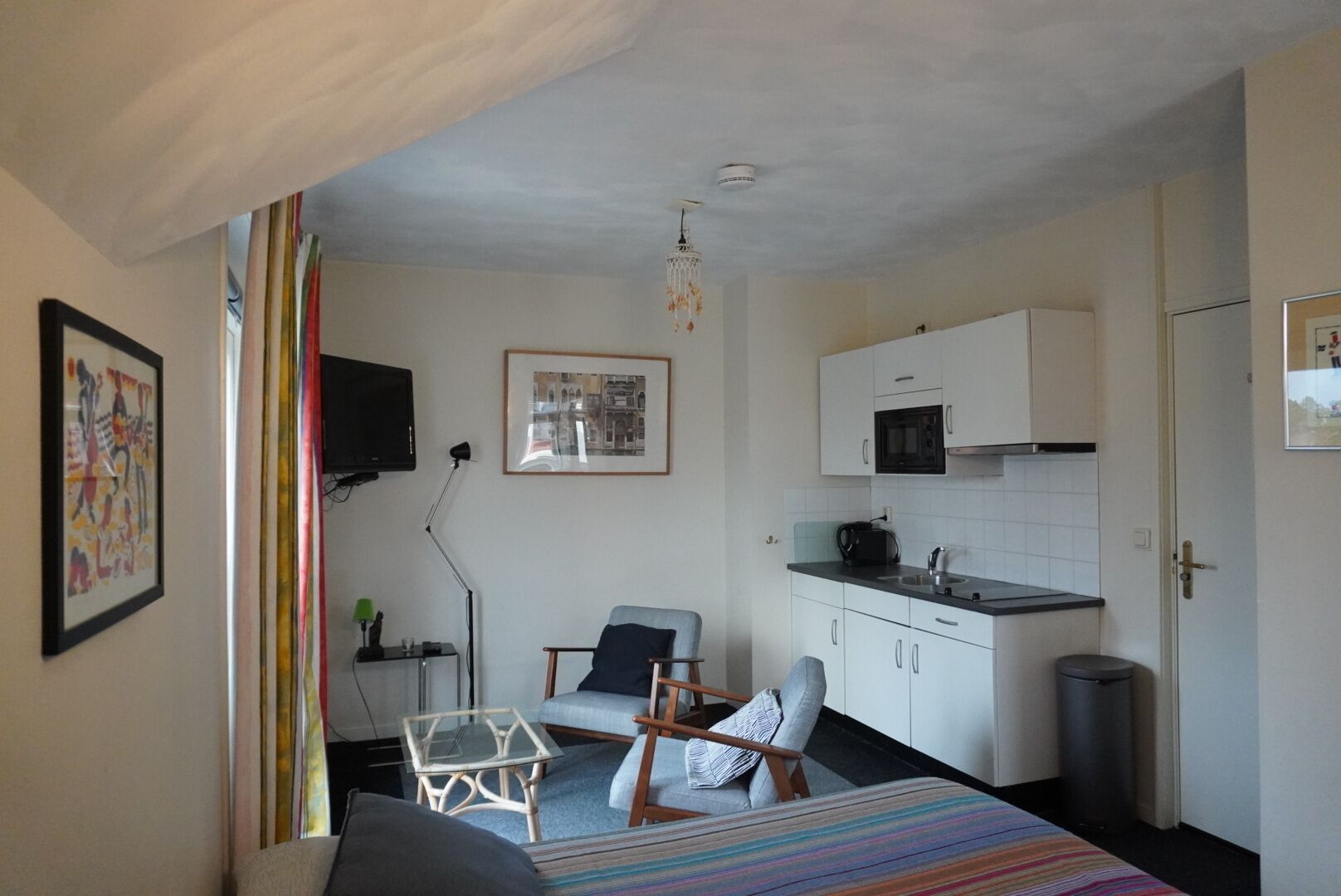 Una camera d'albergo compatta con un letto, un tavolino, una sedia, angolo cottura e televisione.