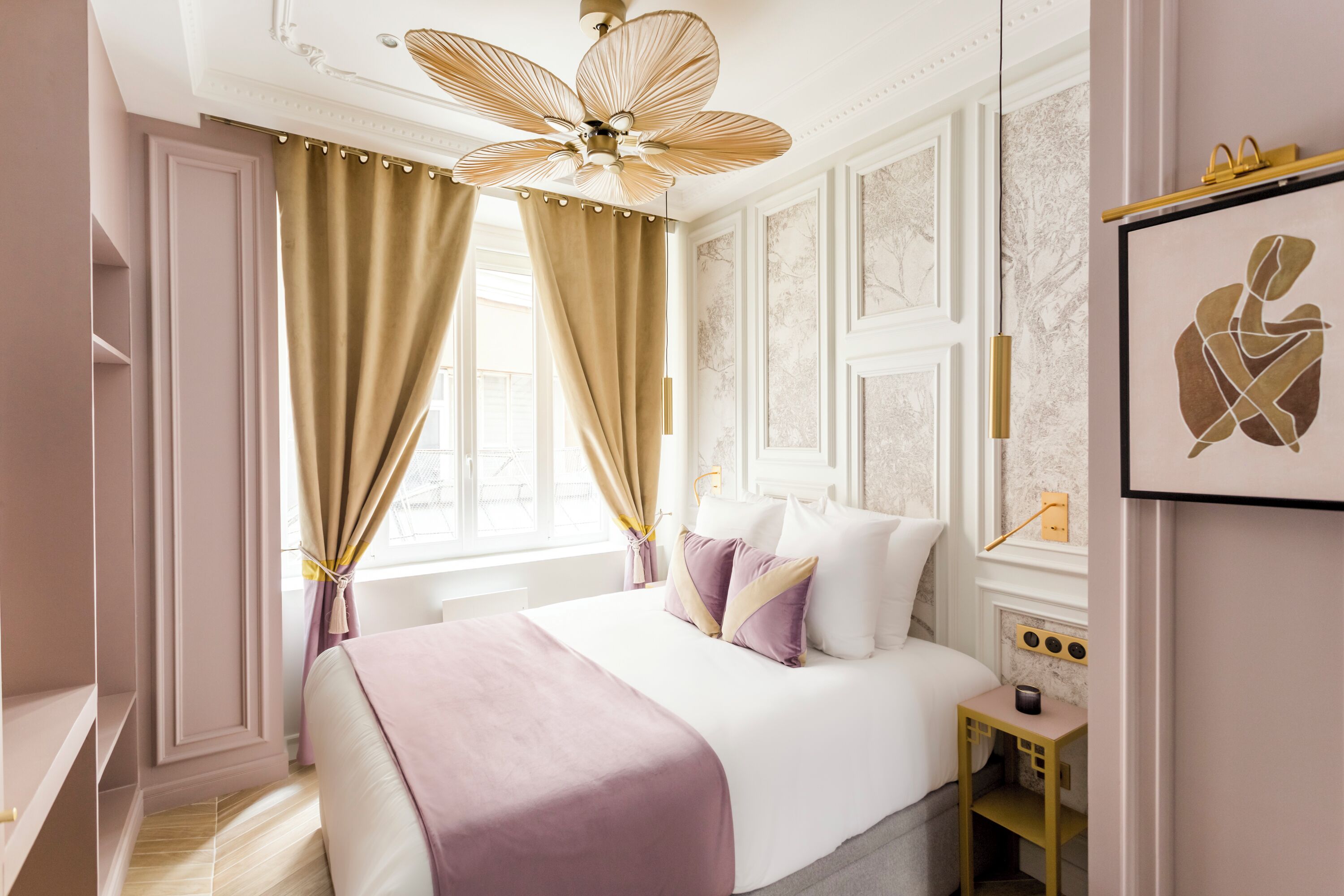 Een slaapkamer met een bed, gordijnen, een plafondventilator, een nachtkastje en een lijst met een afbeelding aan de muur.