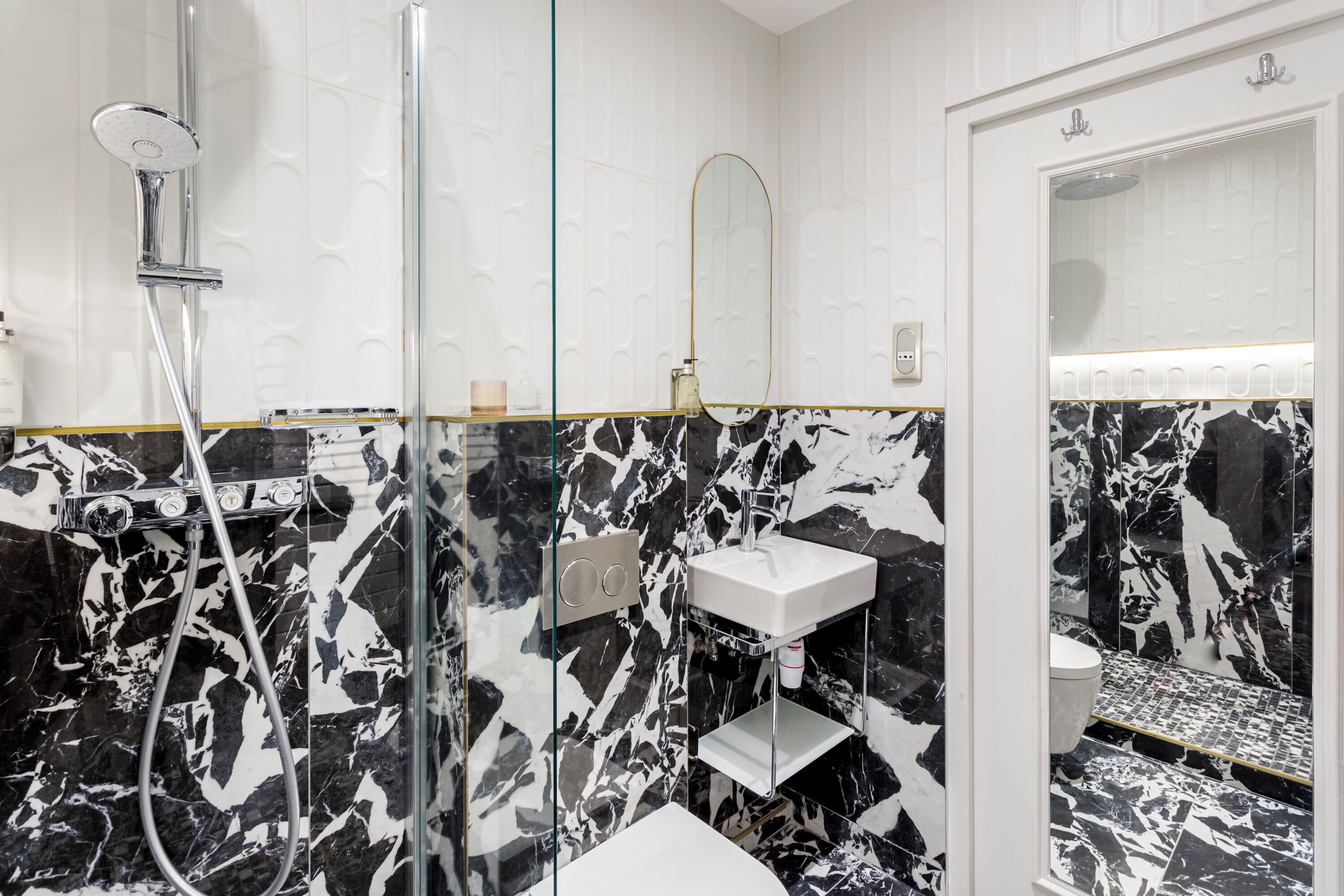 A modern bathroom with a glass-enclosed shower, a white sink, and a marble-patterned wall.