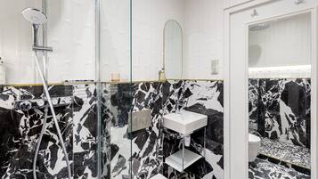 A modern bathroom with a glass-enclosed shower, a white sink, and a marble-patterned wall.